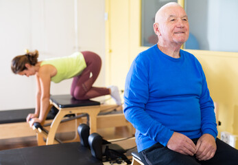 Portrait of an elderly senior citizen in a rehab room doing pilates