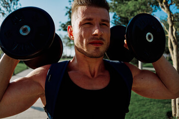 athletic man with dumbbells in his hands in the park training lifestyle