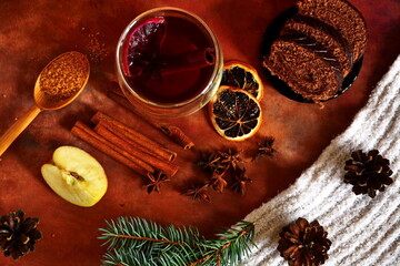 winter warm drink with cinnamon, star anise and lemon with chocolate roll and spoon of brown sugar. Top view on table decorated with spices and herbs, apple slice, fir cones and branch on scarf