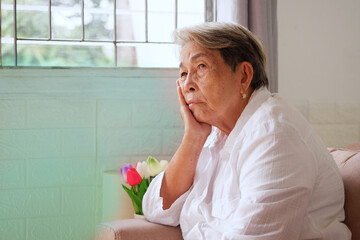 Elderly Asian woman with grey hair sits on her chin with a sad expression. Aging society Sad and lonely concept, with copy space for text.