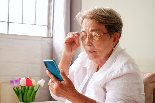 Elderly Asian woman with grey hair is using a mobile phone and holding her glasses. Eye problems in the elderly, blurry vision, concept