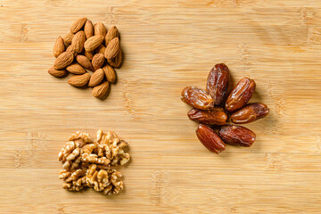 Raw almonds, organic pitted dates and walnut halves on the wooden cutting board background