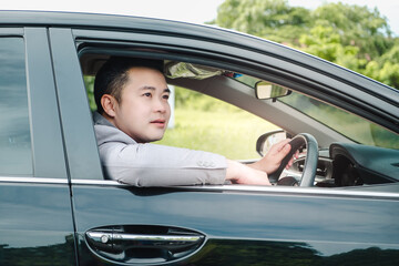 Happy businessman while driving the car and smiling on his morning commute to work. Executive handsome Asian young man on his luxury automobile on the road trip.
