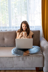 A young woman is drinking a cup of coffee during working from home.