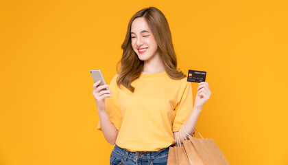 Beautiful Asian woman holding brown blank craft paper shopping bags and showing credit card on yellow background.