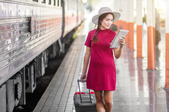 Asian woman pregnant in red dress holding a map with red suitcase  at railway station travel,traveler with backpack in summer Holiday concept Thailand