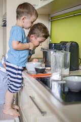 Two cheerful male children cooking homemade baking dessert together mixing ingredients for dough