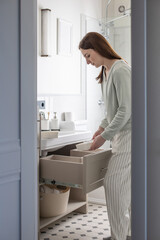 Housewife hands putting rolled up towel into drawer under sink. Organizing storage space in bathroom