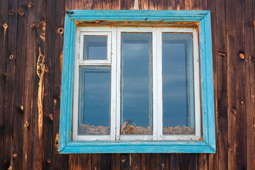 Old Russian window in wooden wall with layer of dry grass between the glass panes. Horizontal image.