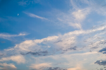Blue sky background with white and pink clouds and moon at sunset