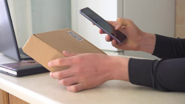 Attaching a QR code to delivery or package. A man using a smartphone and an application scans the QR code on the parcel box