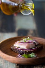 Homemade Borodino rye bread with herring and onions is poured with butter on a wooden bowl. Front view.