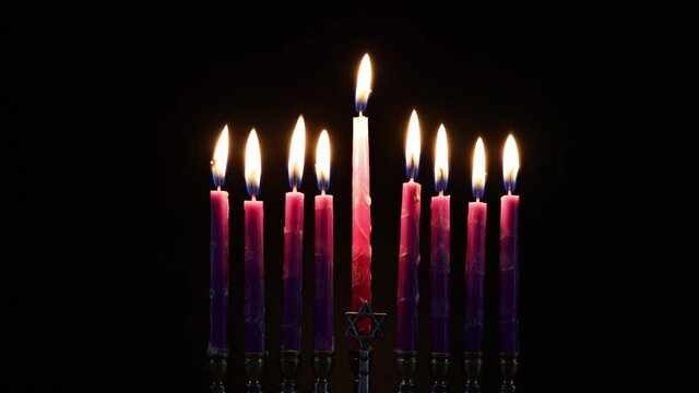 Close up burning pink candles on menorah on black background. Jewish holiday Hanukkah symbol.