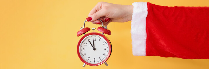 Red alarm clock holds hand in santa claus costume closeup