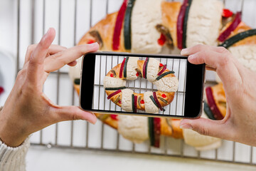 mexican woman baking a traditional rosca de reyes or epiphany cake and taking photo with mobile phone in kitchen at home for Kings Day in Mexico Latin America