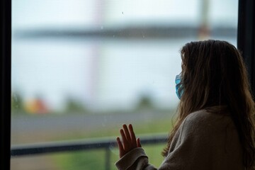Girl in mask, looking through window, wanting to go outside.