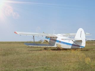 An old Soviet plane white with a blue stripe is standing in a field at the airfield