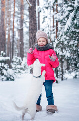 Fototapeta na wymiar Little girl in a bright jacket plays in the winter snowy forest with her dog