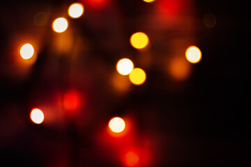 Multi-colored bokeh on a black background. Bright blurry textures of holiday lights. Colorful beautiful Christmas garlands on blurry background. Layout of a greeting card for the New year. Copy space