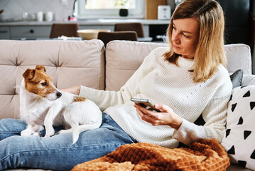Woman resting on sofa with her dog and using smartphone