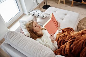 Woman relaxing on couch and reading book at home