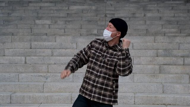 Asian man in medical mask dancing on background of concrete stairs close-up.