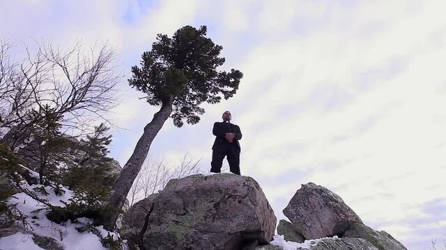 the priest preaches on the mountain. A man in the clothes of a pastor stands on a stone. Winter and cold in the mountains