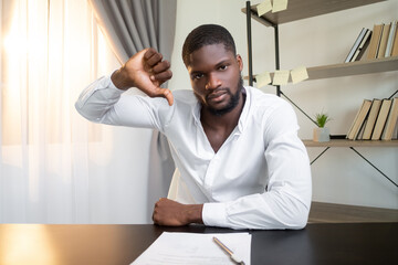Fototapeta premium Contract reject. Offer disapproval. Project failure. Dissatisfied frown business man refusing deal with thumb down bad gesture at office workplace interior.