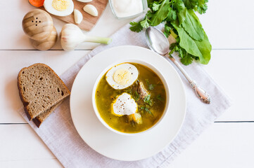 on a white wooden bowl table with spring vegetable soup of sorrel with sour cream and chicken egg. top view.