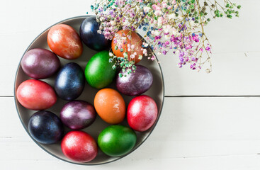 a large dish with colorful Easter eggs and flowers on a white wooden background. top view. traditional Easter treats.