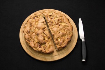Juicy apple pie, cut with a knife, on a dark background, close up