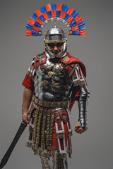 Proud roman soldier posing against gray background holding sword