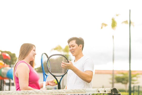 Hombre asiático explicando a una mujer caucásica, cómo utilizar las raquetas para jugar tenis 