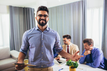 Businessman leader holding digital tablet in modern office with businessmen working at the background.