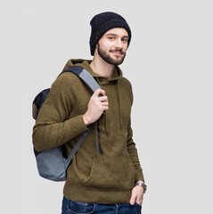 Young handsome man with backpack isolated on gray background. Smiling student or businessman winter...