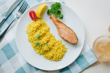 proper nutrition, daily diet, weight loss. greens, tomatoes, salmon steak with lemon and couscous garnish on a plate. Top view