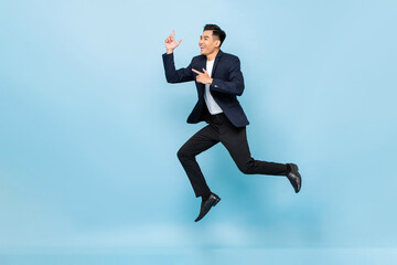 Full lenght portrait of smiling handsome Asian man jumping and pointing hands up on isolated light blue studio background