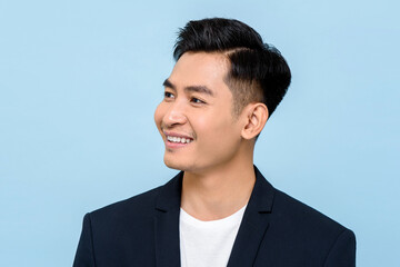 Young Asian man smiling and looking sideways in isolated light blue color background