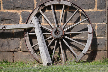 Fototapeta na wymiar old wagon wheel against bluestone wall