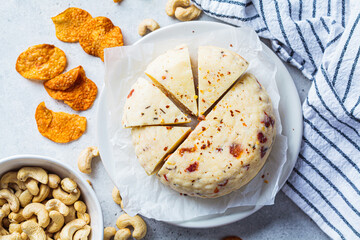 Vegan cashew cheese with dried tomatoes and spices on white plate, gray background. Alternative...