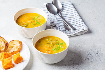 Homemade broccoli cheddar cheese soup with green onions in white bowl, gray background. Vegetarian food concept.