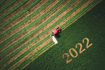2022 Happy New year concept and red tractor mowing green field - obrazy, fototapety, plakaty