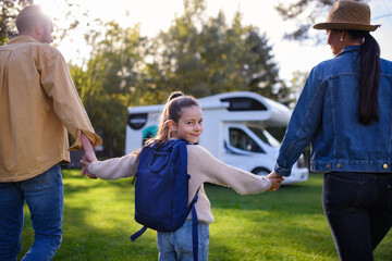 Rear view of little girl looking at camera and holding parents when going to caravan outdoors at park. - obrazy, fototapety, plakaty
