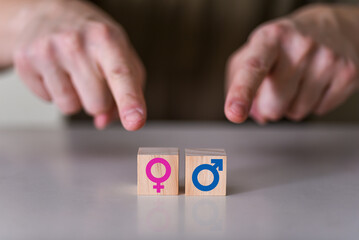 A choice between a man and a woman. the hands point to two wooden cubes with a gender icon, a male and a female sign.