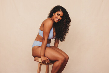 Cheerful young woman sitting comfortably in blue underwear - obrazy, fototapety, plakaty
