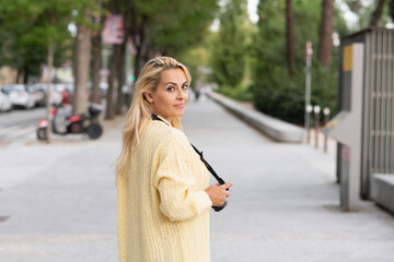 Woman turning to look at the camera while holding a photo camera outdoors