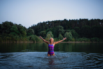 Happy active senior woman swimmer splashing water outdoors in lake.
