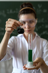 Woman chemistry teacher  mixes liquids in a glass flask against blackboard