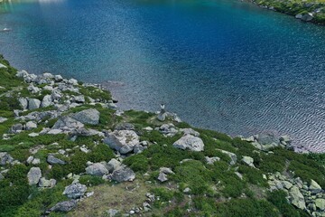 Aerial drone view of alone woman traveler in dress and hat watching on Seven colored mountain glacial lake, summer landscape: high peaks, snow, stones. Arkhyz, Caucasus, Karachay-Cherkessia, Russia
