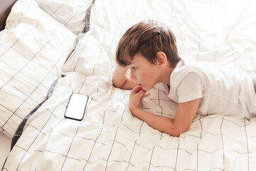 Child sitting relaxed in bed and playing on smartphone